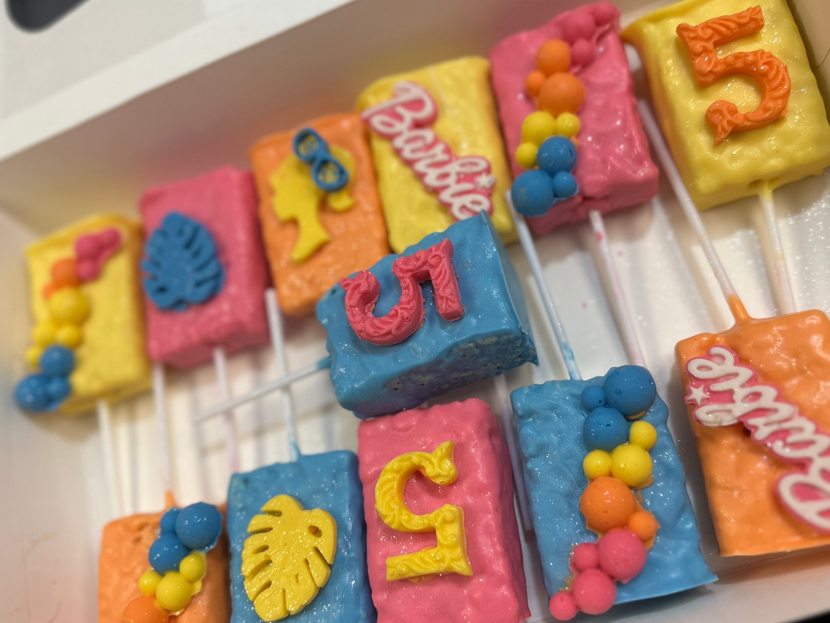 Colorful cake pops with letters and 'Barbie' branding in a box.